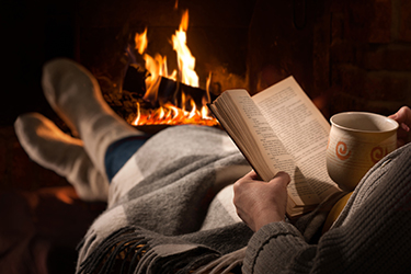 A person reading a book by a fireplace