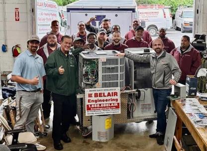 The Belair team gathered around an AC condenser and water heater display in the company shop